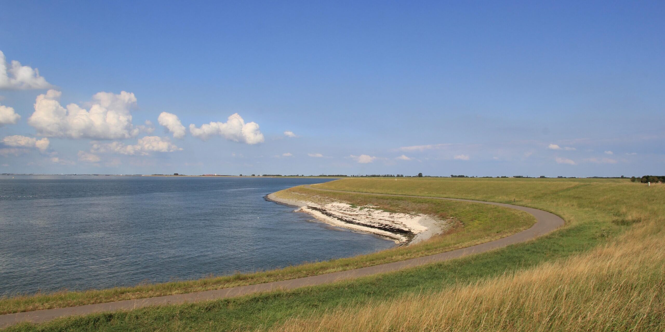 beautiful seascape of the westerschelde sea with high tide and the green dike with road and heavenly blue sky at a clear sunny day in summer